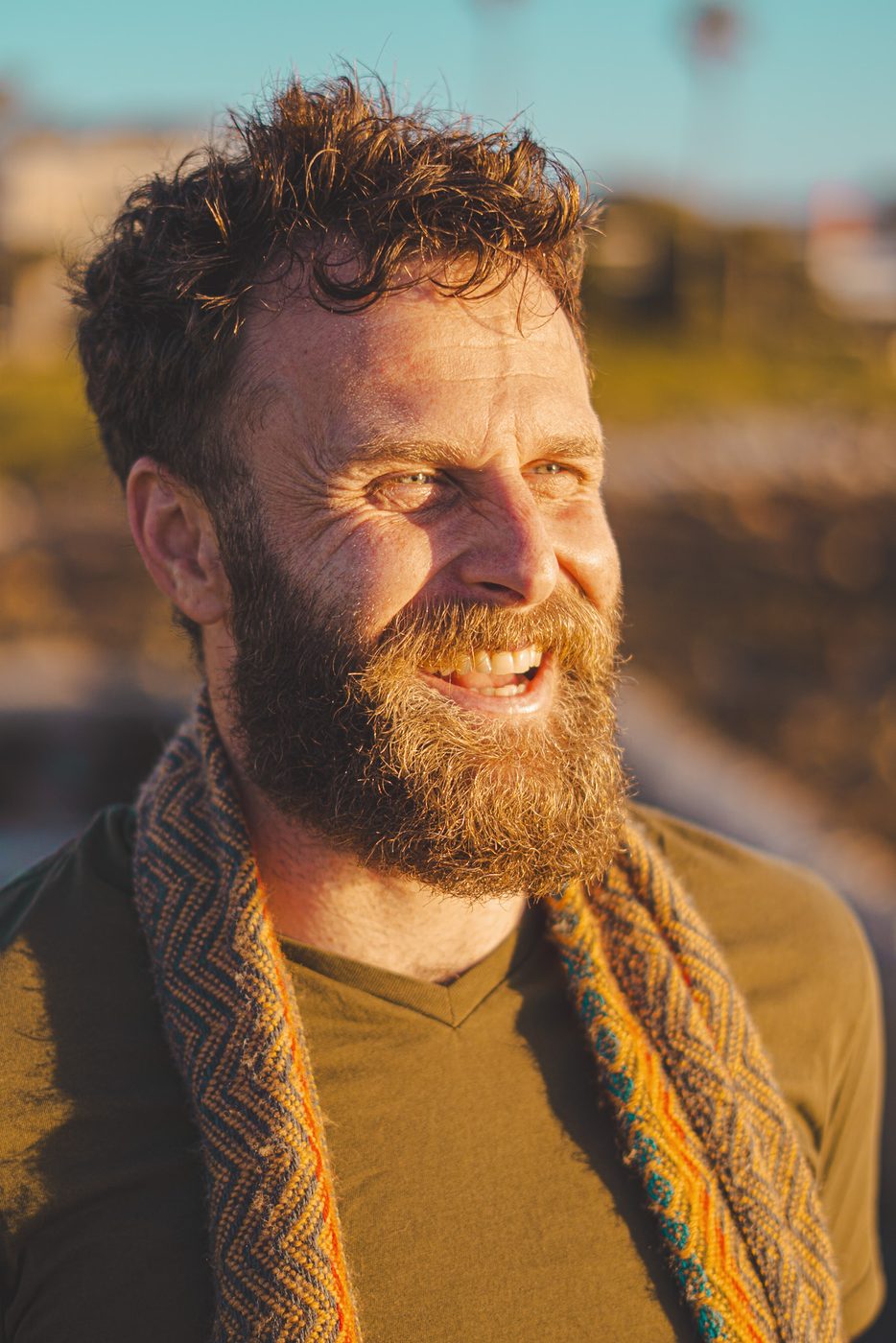 Nathan Maingard smiling in golden evening light, wearing a woven scarf