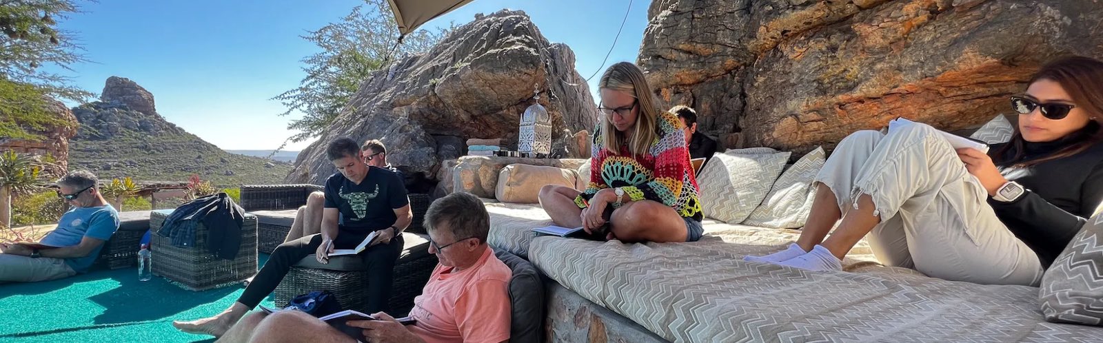 Leadership group writing and reflecting together beside the pool at Planet Xancara, dramatic rock formations behind them