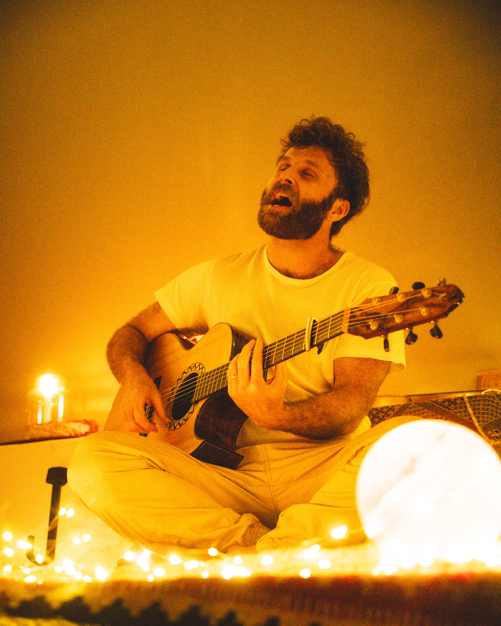 Nathan Maingard singing by candlelight with an acoustic guitar